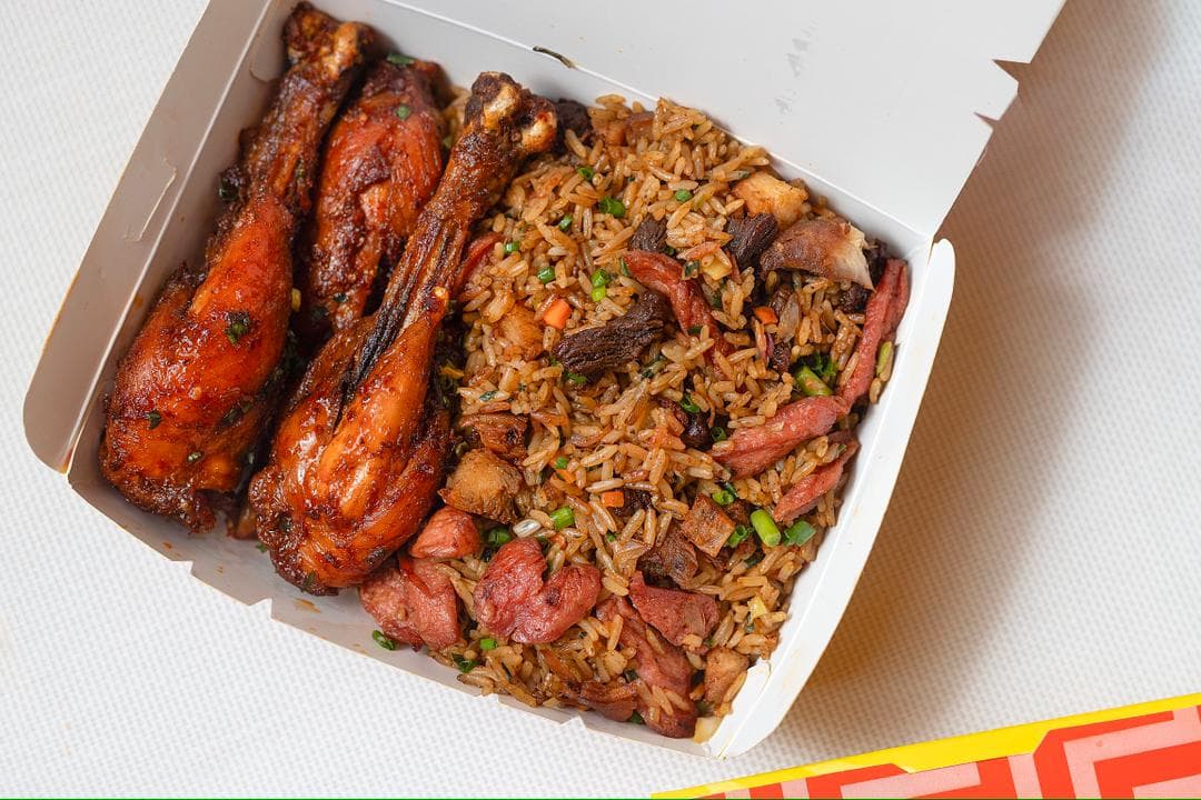 A takeaway box of fried rice with three chicken drumsticks